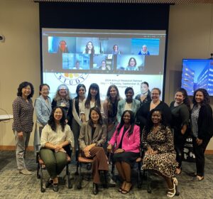 Photo of a group of smiling people in front of a presentation screening with Zoom attendees at the ACHIEVE Study's 2024 Annual Research Retreat